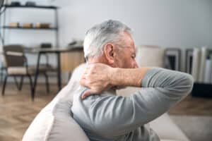 Man sitting on a sofa chair and rubbing his neck in pain