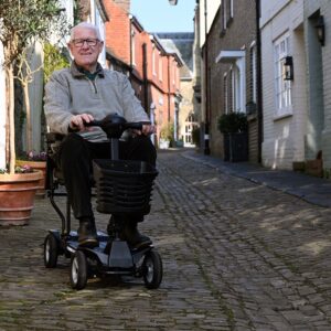 Man sitting on Mirage folding mobility scooter on cobble street