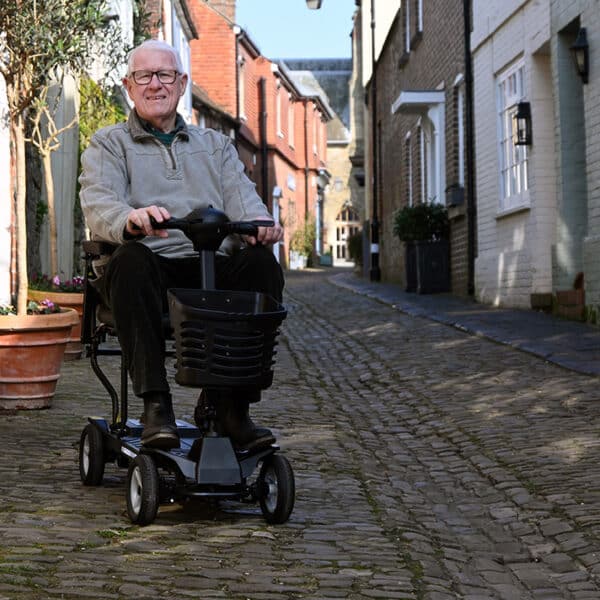 Man sitting on Mirage folding mobility scooter on cobble street